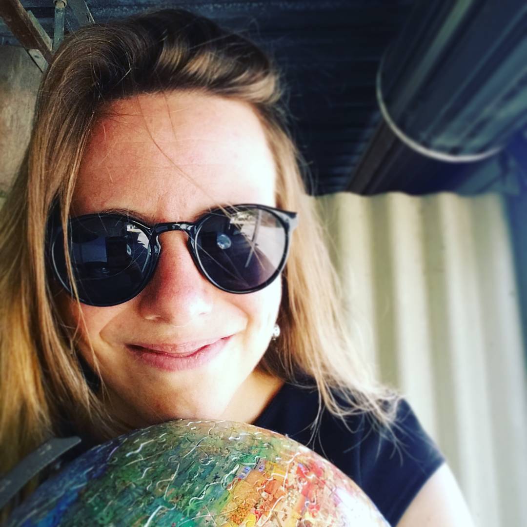 Image of Maya's head, wearing sunglasses with her chin resting on a puzzle Earth globe.